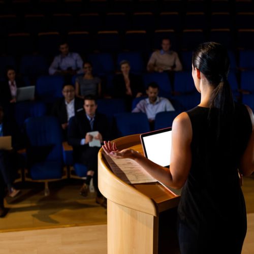 vista-traseira-do-executivo-de-negocios-feminino-dando-um-discurso (2) (1)